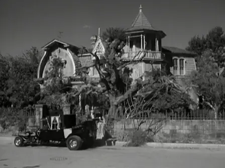The Munsters beside the Munster Koach on the street in front of their house